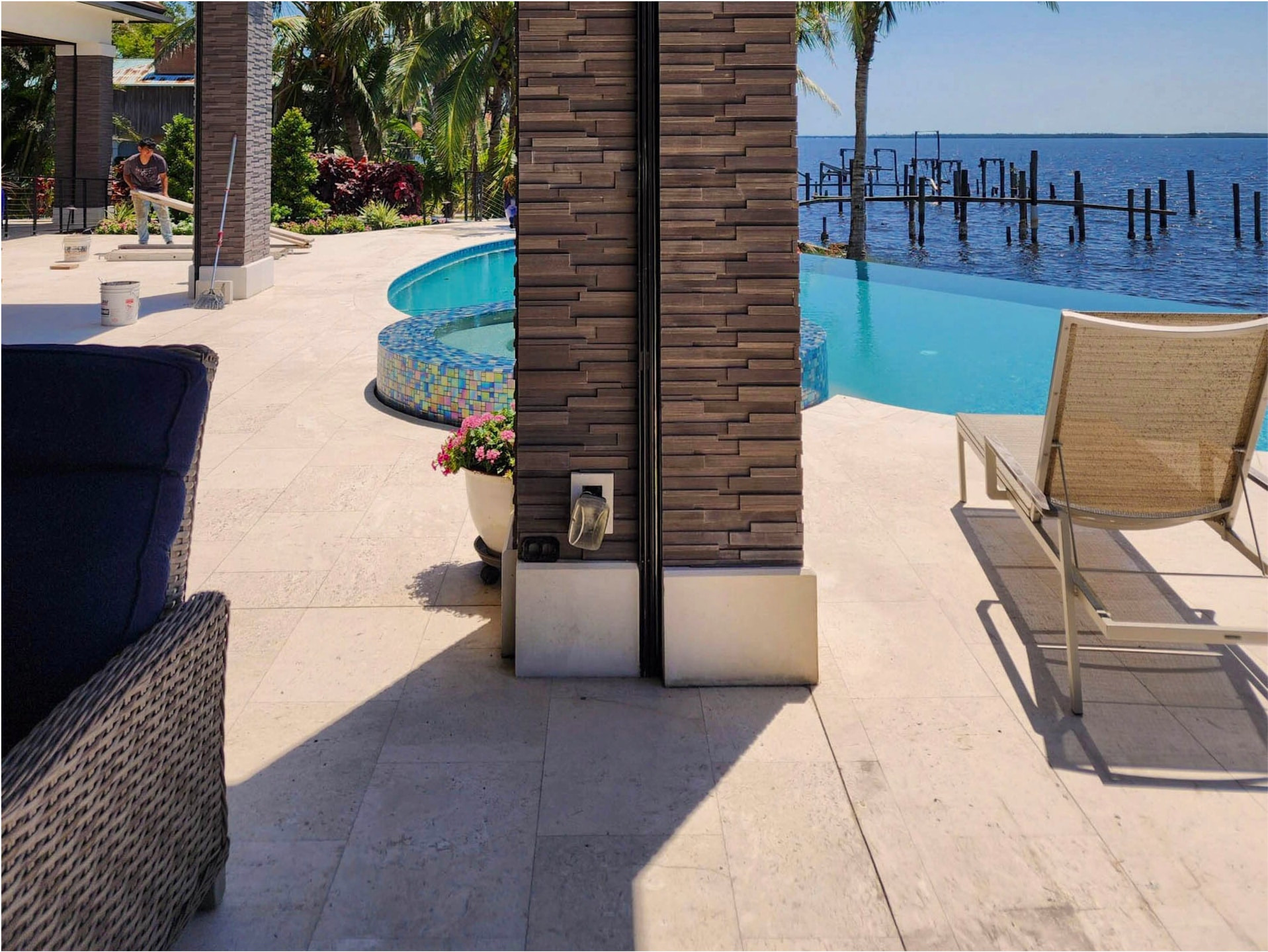 JBA pool coping installed on a Naples bayfront — travertine, stacked-stone column, infinity pool